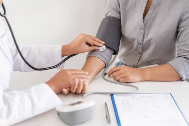 Doktor, hastayı steteskopla, tansiyon monitörüyle muayene eder ve sonuçları kaydeder..