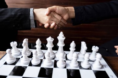 Beyaz arkaplanda satranç oynamadan önce el sıkışan iş kadınları, başarı konseptine iş stratejisi planlamakta güçlük çekiyor.