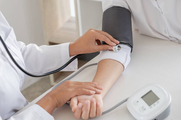 Doctor evaluates the patient with a stethoscope, blood pressure monitor and records the results.