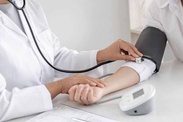 Doctor evaluates the patient with a stethoscope, blood pressure monitor and records the results.