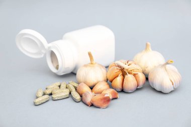 Sarımsak, sarımsak tableti, gri arka planda beyaz ilaç şişesi. Alternatif tıp, bitkisel tedavi kavramları.