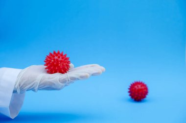 Laboratuvar personeli kırmızı topu mavi arka planda virüs gibi tutuyor..