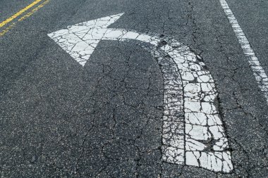 A left turn only arrow painted white on the asphalt cracked and worn away by traffic on the street outdoors clipart