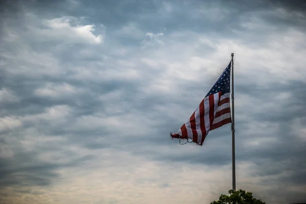 背景に鳥が旋回する嵐の空に誇らしげに飛ぶ大きなアメリカの旗が裂けて引き裂かれました — ストック写真