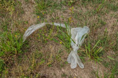Kullanılmış plastik bir eldiven ve yanında bir plastik parçası var. Çimlere dökülmüş. Coronavirus 'a karşı koruma sağlıyor.
