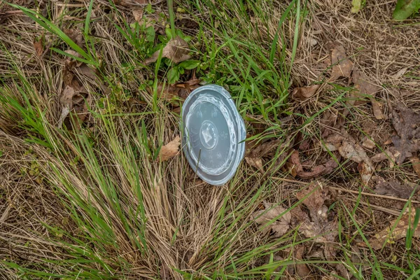 A plastic to go cup lid laying on the ground in the grass alongside the highway thrown and discarded garbage