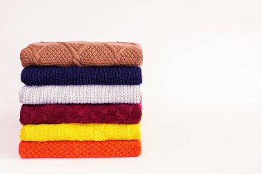 Multicolored warm knitted clothes stacked in a pile on a white background