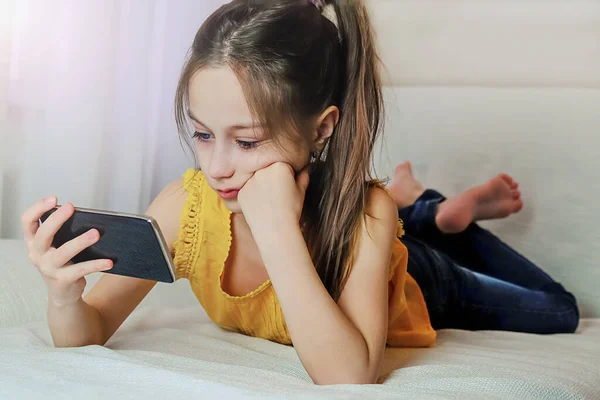 Dziewczyna ogląda film w domu iPhone 'a leżącego na kanapie — Zdjęcie stockowe