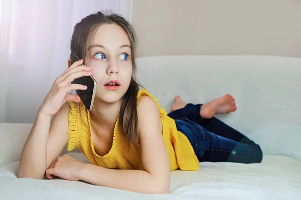 Dziewczyna mówi na iPhone wyrażając emocje z ogromnymi oczami w domu na kanapie — Zdjęcie stockowe