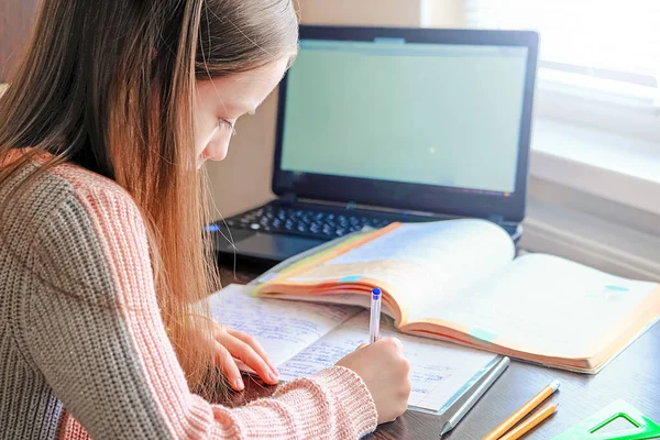Chica sentada en el escritorio haciendo lecciones con portátil cerca de la computadora portátil — Foto de Stock
