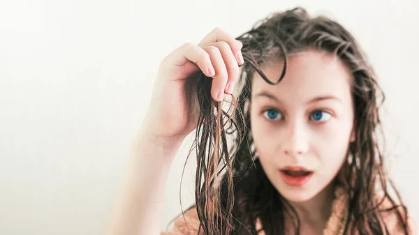 Girl looks at tangled wet hair with surprise