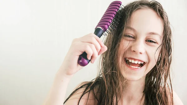 Happy teen girl combs wet hair with smile