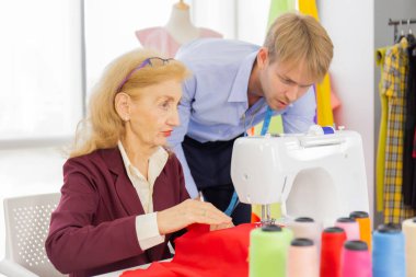 Profesyonel takım tasarımcıları, genç erkekler ve yaşlı kadınlar çeşitli kumaş tonlarıyla ve çeşitli tasarımlar için ekipmanlarıyla ofiste..