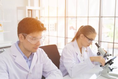 Sağlık araştırmacısı konsepti, yaşam bilimi laboratuvarında çalışan bir araştırmacı, genç bir araştırmacı ve bir erkek denetmen bir araştırma laboratuvarında mikroskobik slaytları hazırlayıp analiz ediyorlar.