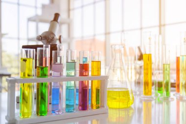 Masanın üzerinde kimyasal reaktör şişeleri, çeşitli şekillerde bilimsel deney şişeleri, boyutlar ve mikroskoplar var.