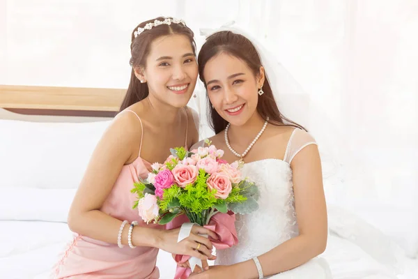 白いウェディングドレスのアジアの花嫁とピンクのドレスの新婦付添人が一緒にバラの花束を持っていて 明るく笑っています — ストック写真