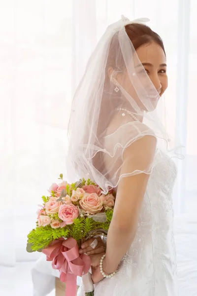 一位亚洲新娘穿着一件白色婚纱 站在她身后 手里拿着一束美丽的花朵 — 图库照片