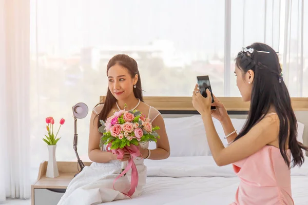 신부의 친구는 스마트폰으로 드레스를 아시아 신부의 사진을 침대에 아름다운 꽃다발을 — 스톡 사진
