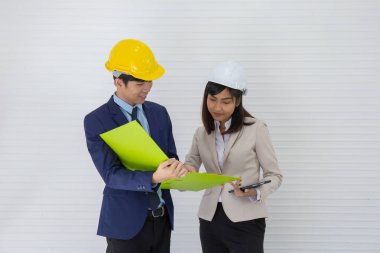 İki Asyalı erkek ve kadın ustabaşı kask takıyor ve olay yerinde dikilip konuşuyorlar.