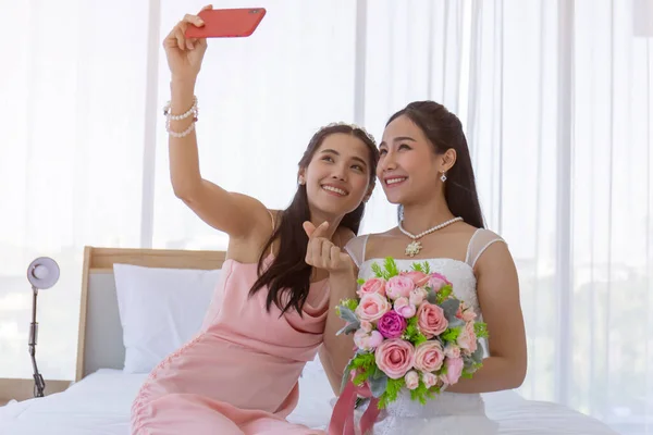신부의 친구는 스마트폰으로 아름다운 꽃다발을 아시아 신부의 셀카를 침대에 드레싱 — 스톡 사진