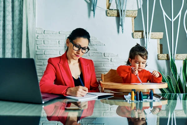 young executive woman working from home while taking care of her young daughter