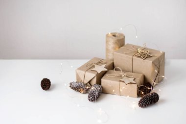 Beyaz arka planda Kraft kağıdındaki hediyeler. Dekor köknar kozalakları, tahta yıldızlar, yeşil ip..