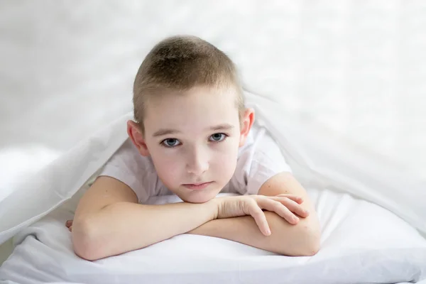 Um menino sério jaz em um travesseiro e embrulhou a cabeça em um cobertor — Fotografia de Stock