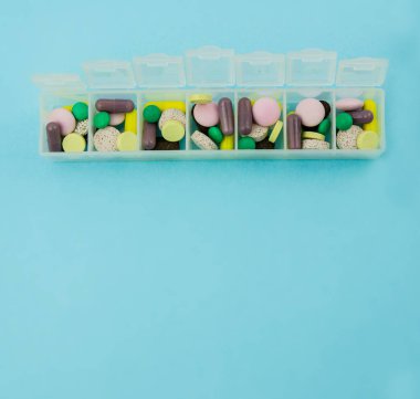 Haplar ve vitaminlerle dolu bir hap kutusu. Yukarıdan bak. Mavi arka planda plastik hap kutusu.