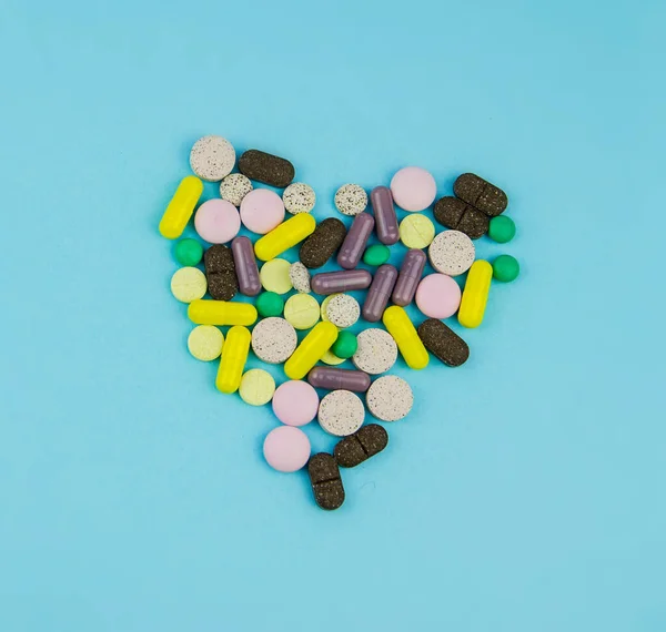 Multi-colored pills, capsules, vitamins laid out in the form of a heart on a blue background. Shot from the top.