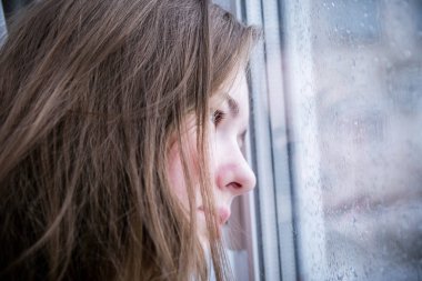 Close up face of teenage girl. The girl clung to the window with raindrops and was sad. The concept of sadness, sadness, loneliness, teenage depression. clipart