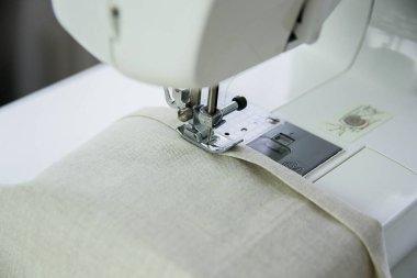 Beyaz bir masa üzerindeki modern bir dikiş makinesi keten kumaştan dikilmiş..
