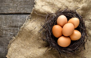 Kırsal ve doğal bir Paskalya. Eski ahşap bir arka planda çuval bezi üzerinde dalların olduğu bir yuvada yumurtalar. Boşluğu kopyala.