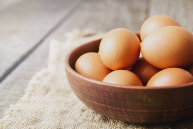 Çuval bezinde kilden bir tabakta ve eski ahşap bir arka planda yumurtalar. Boşluğu kopyala.