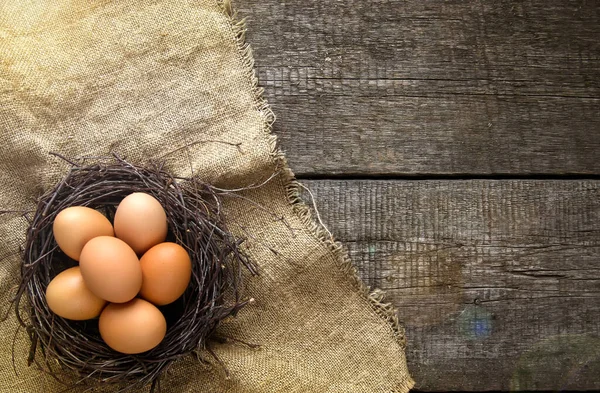 Kırsal ve doğal bir Paskalya. Eski ahşap bir arka planda çuval bezi üzerinde dalların olduğu bir yuvada yumurtalar. Boşluğu kopyala.