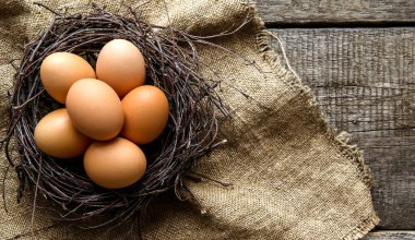 Kırsal ve doğal bir Paskalya. Eski ahşap bir arka planda çuval bezi üzerinde dalların olduğu bir yuvada yumurtalar. Boşluğu kopyala.