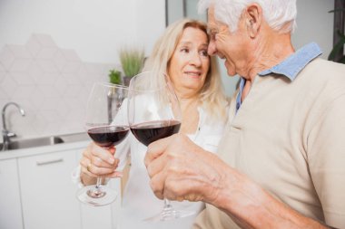 Mutlu son sınıf çifti evde mutfakta konuşurken ve kırmızı şarap içerken rahatlıyor.