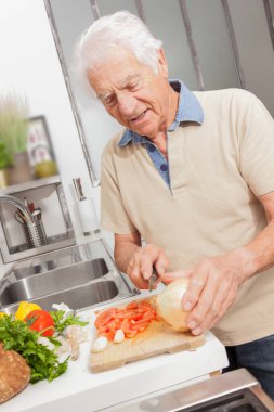 Evdeki bir mutfakta sağlıklı yiyeceklerle yemek pişiren mutlu kıdemli bir adam. Beyaz saçlı adam sebze doğradı.