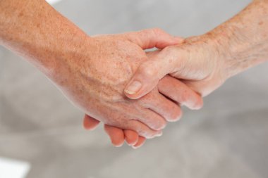 Genç bir kadın son sınıf kadınının elini tutuyor, yakın plan. İki nesil arasında şefkatli bir jest..