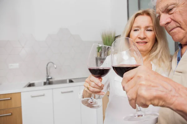 Happy senior couple relax talking and drinking red wine glasses together in the kitchen at home