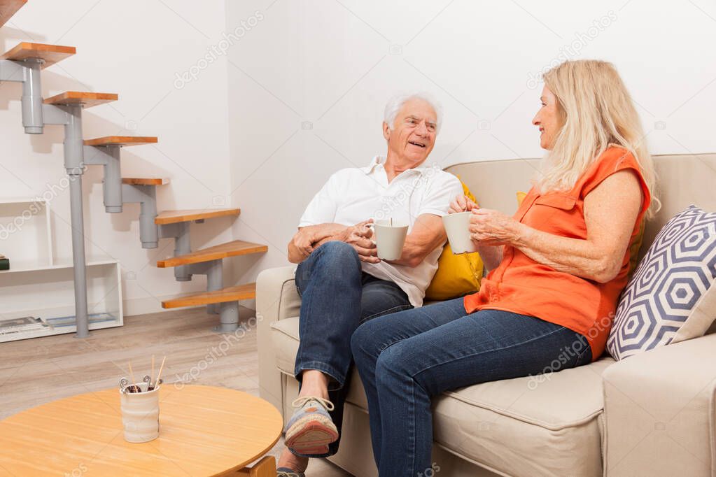 Happy senior couple drinking a tea, sitting on sofa in living