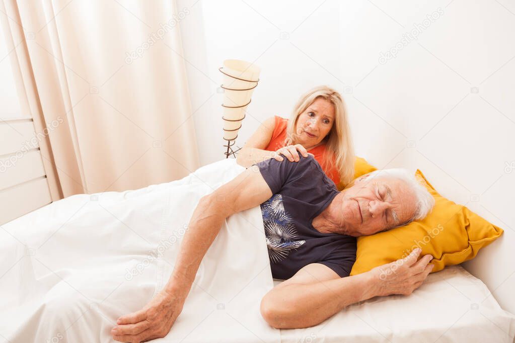 Senior couple in bed. Man sleeping et dreaming. Woman is awake in the bedroom
