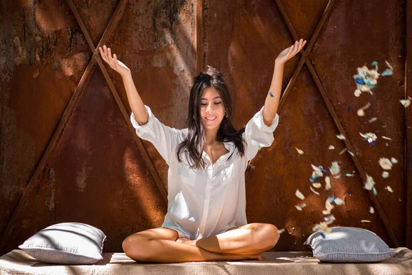 Bahçede yoga yapan gülümseyen genç bir kadın. İç huzuru bulmak. Pozitif enerji. Özgürlük için. Rahatlama. Meditasyon. Kız bacak bacak üstüne atmış, tomurcuk yapraklarıyla oturuyor.