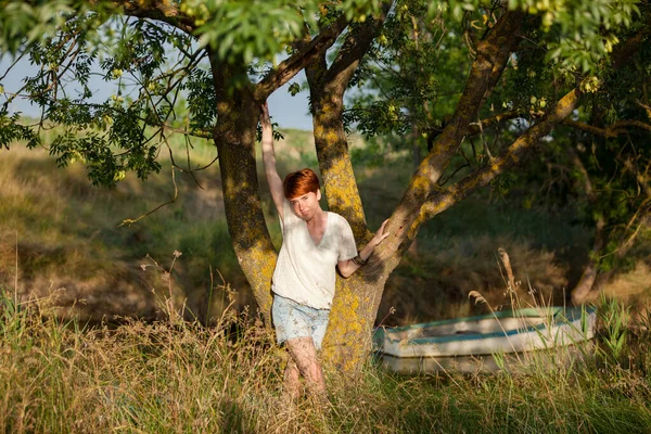 WELL-BEING, WOMAN AGAINST A TREE IN THE GRASS IN THE COUNTRYSID