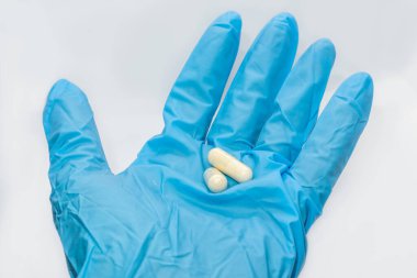 Mavi eldiven, beyaz arka planda uzun kapsüller alır. İlaç ilacı hafif renkler makro izole yakın çekim