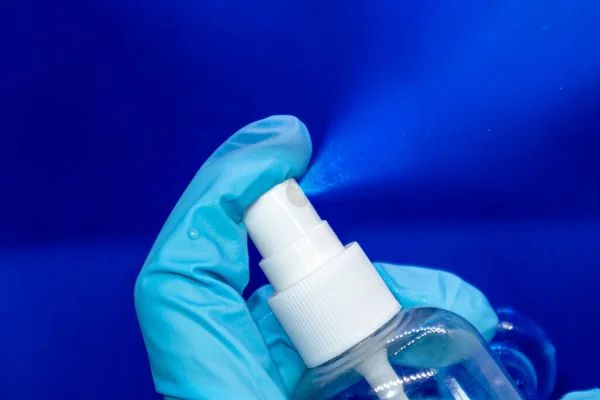 Spray disinfect liquid, hand in blue glove on blue background. Sanitize spray water drops. Prevent virus illness spread in air aerosol. Clean hands