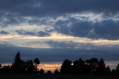 Dramatik gün batımı bulutları koyu bulutlar ve koyu ağaçlı turuncu güneş silueti. Canlı renkler resim gibi.