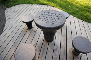 Şehir parkının dinlenme yerinde satranç oynamak için tahta zeminde ve yeşil çimlerde satranç masaları.