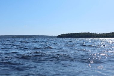 Mavi su temiz gökyüzü güneşli bir günde Finnish Gölü 'nde su dalgaları kapanıyor. Doğanın güzelliği ufuk çizgisi ve derin renkli suyu olan orman. Tekneden fotoğraf.