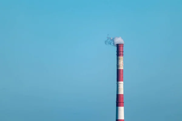 Energy heat power station pipe with red white stripes on blue sky background. Europe, Ukraine industrial air pollution smoke tower.