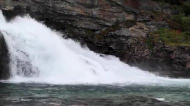 Güçlü beyaz su döngüsü yeşil çalılarla siyah kayaların üzerine düşüyor. Kuzey İskandinavya yazı Norveç doğası harekete geçti. Taze şelale ve doğal taşlar güzellik